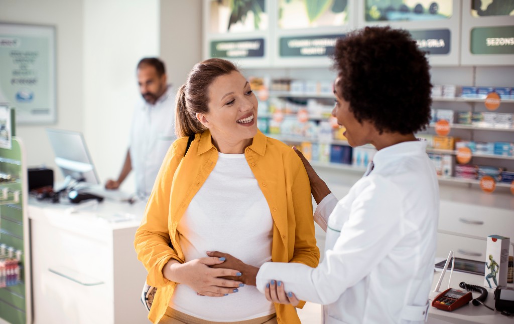 farmacêutica sorridente segurando barriga de grávida em uma farmácia