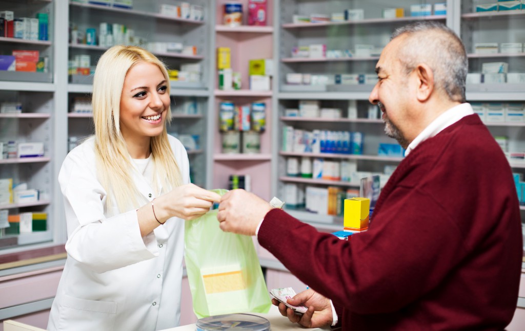 farmacêutica sorridente entregando sacola de medicamentos a um senhor no balcao da farmácia